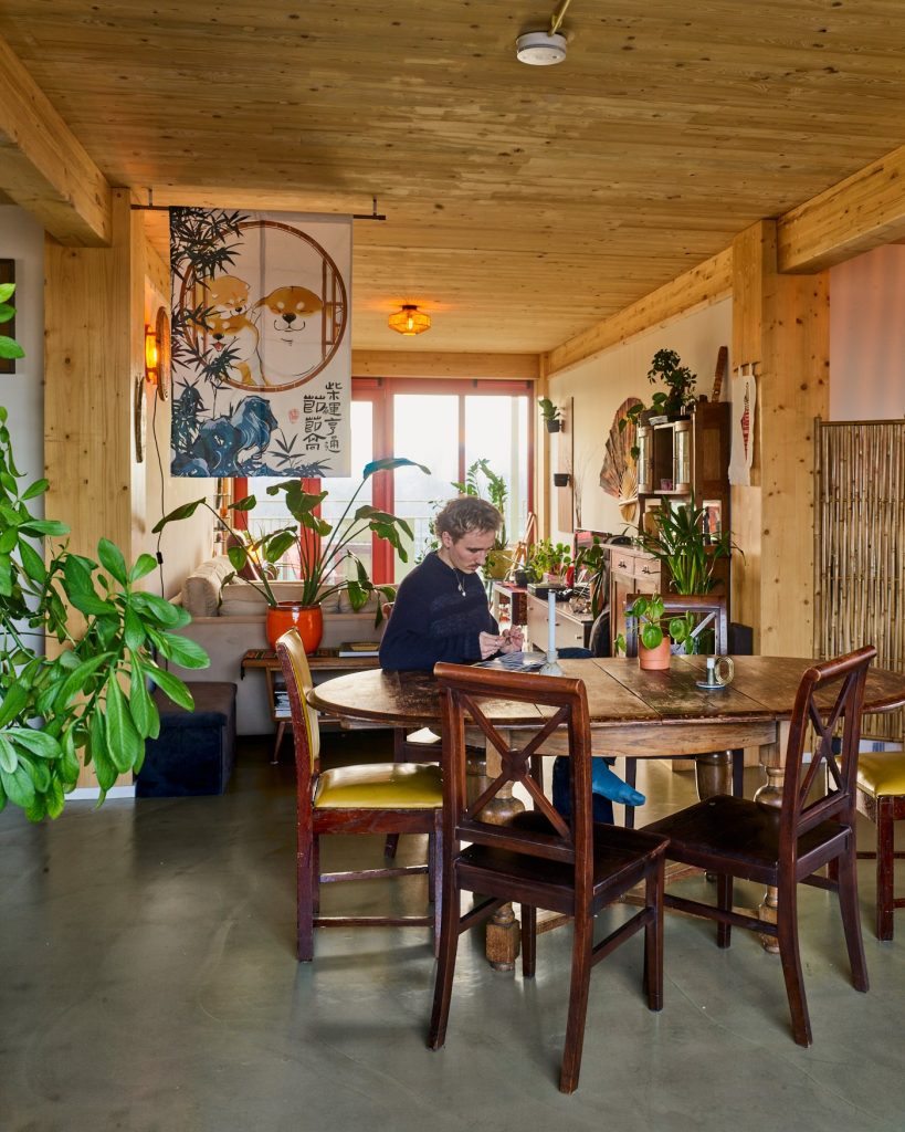 A shared living room in one of the living groups: a long wooden table, plants and a timber ceiling