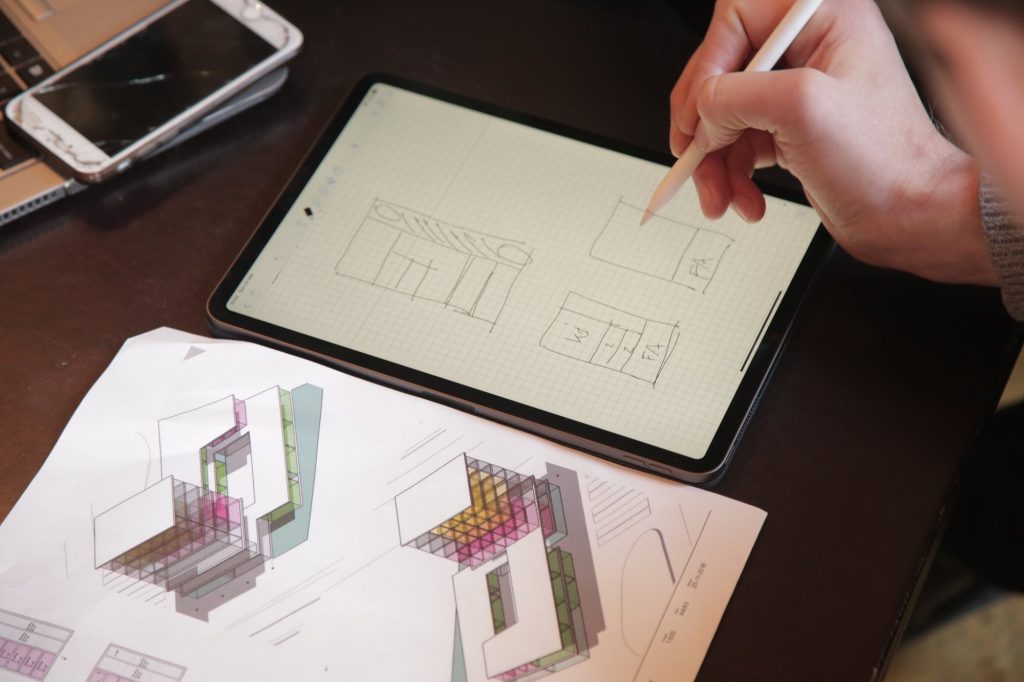 Sketching floor-plan options on a tablet next to printed isometric drawings, at a co-design meeting in March 2019