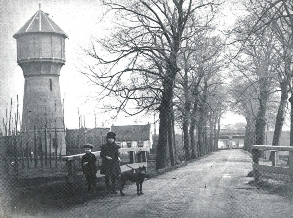 The water tower that stood on our plot, around 1900, with children and a dog on the road in front