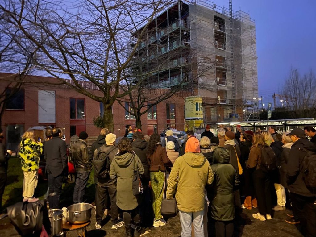 A crowd in front of the building under construction, at dusk