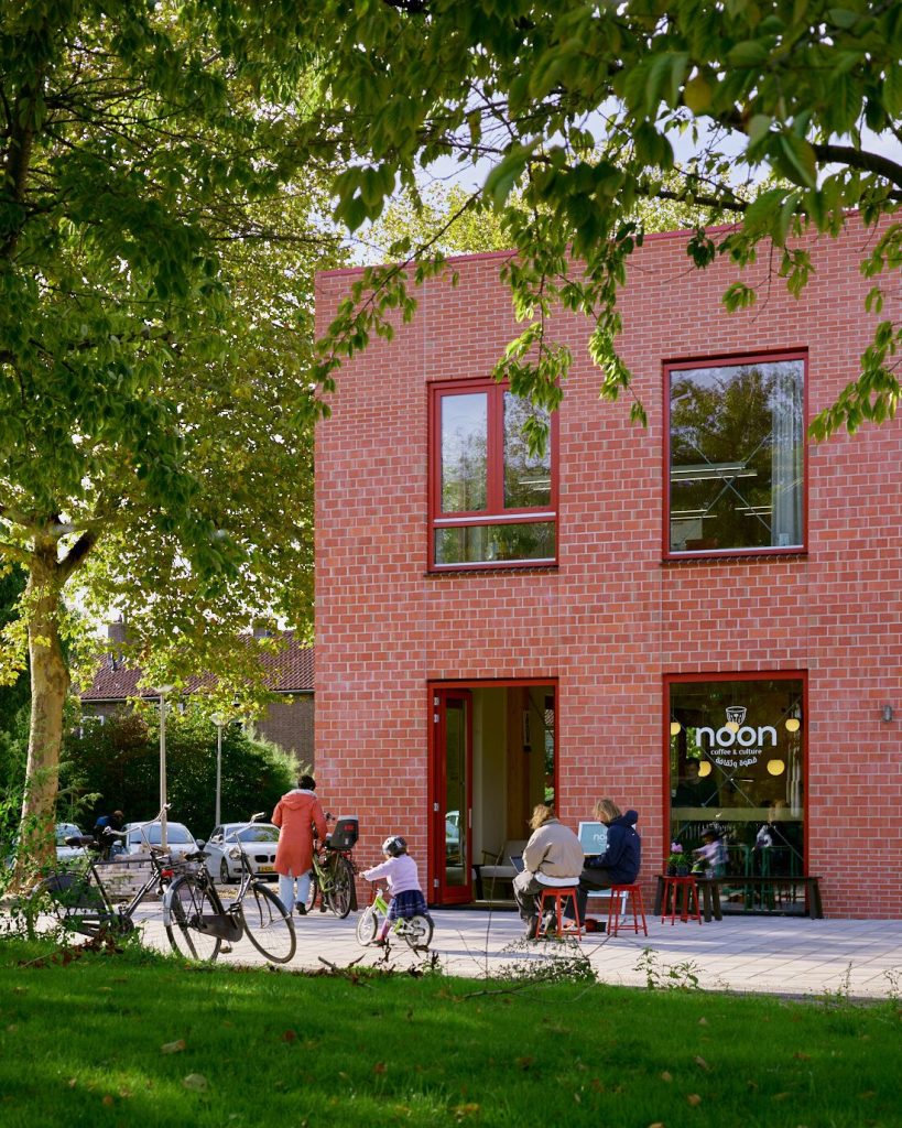 The corner with Noon café under a tree, bikes and neighbours outside
