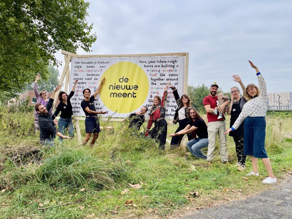 Members waving in front of the de Nieuwe Meent banner on the empty plot