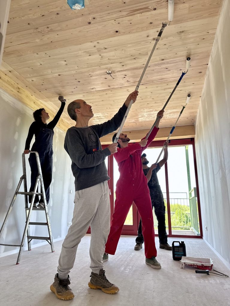 Three residents painting a timber ceiling with rollers